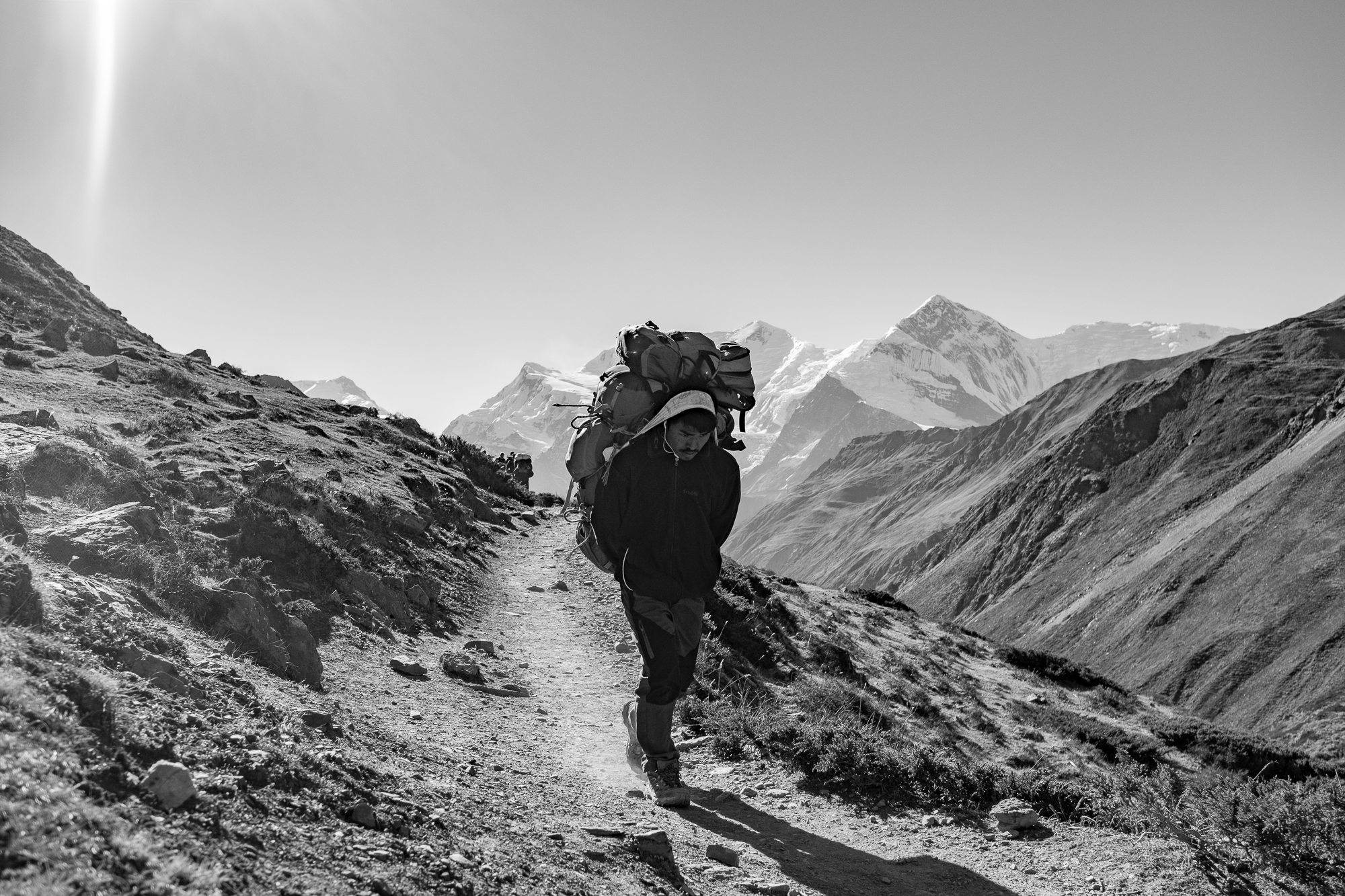 Porter carrying three full hiking backpacks, from Manang up to the lower basecamp. Even if they carry an incredibly heavy load, porters often walk ahead of the group the whole time, at a slow but steady pace.